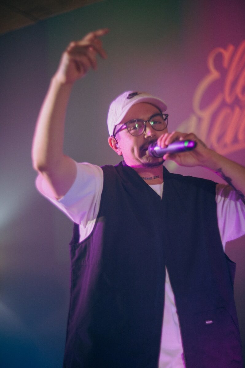 Man in a cap and vest rapping into a microphone